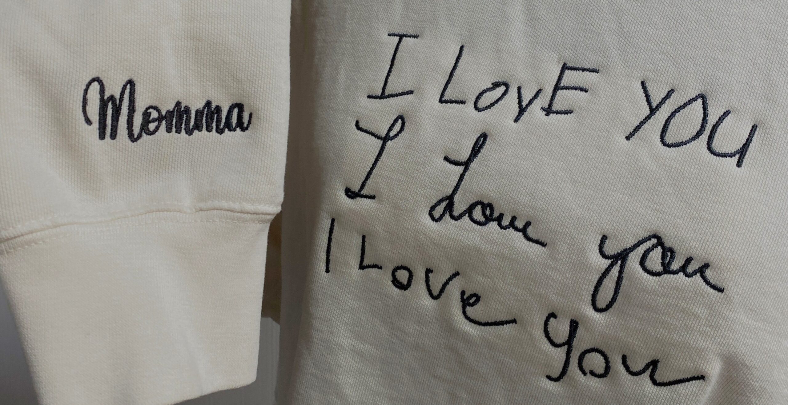 Image shows an embroidered sweatshirt, cream in color, with black thread.  The sweatshirt has "Momma" embroidered on the sleeve and "I love you" embroidered on the front, in three styles of loved ones' handwriting.  This image is merchandise crafted by Sweet Magnolia Boutique, who specializes in the following: Embroidery | Screen Printing | 3D Printing | Vinyl
Custom Branded Merchandise