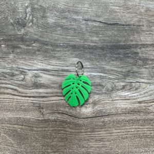 Photo is of a 3D Printed Fidget Keychain with a center cutout shape of a monstera leaf. The keychain color is neon green.