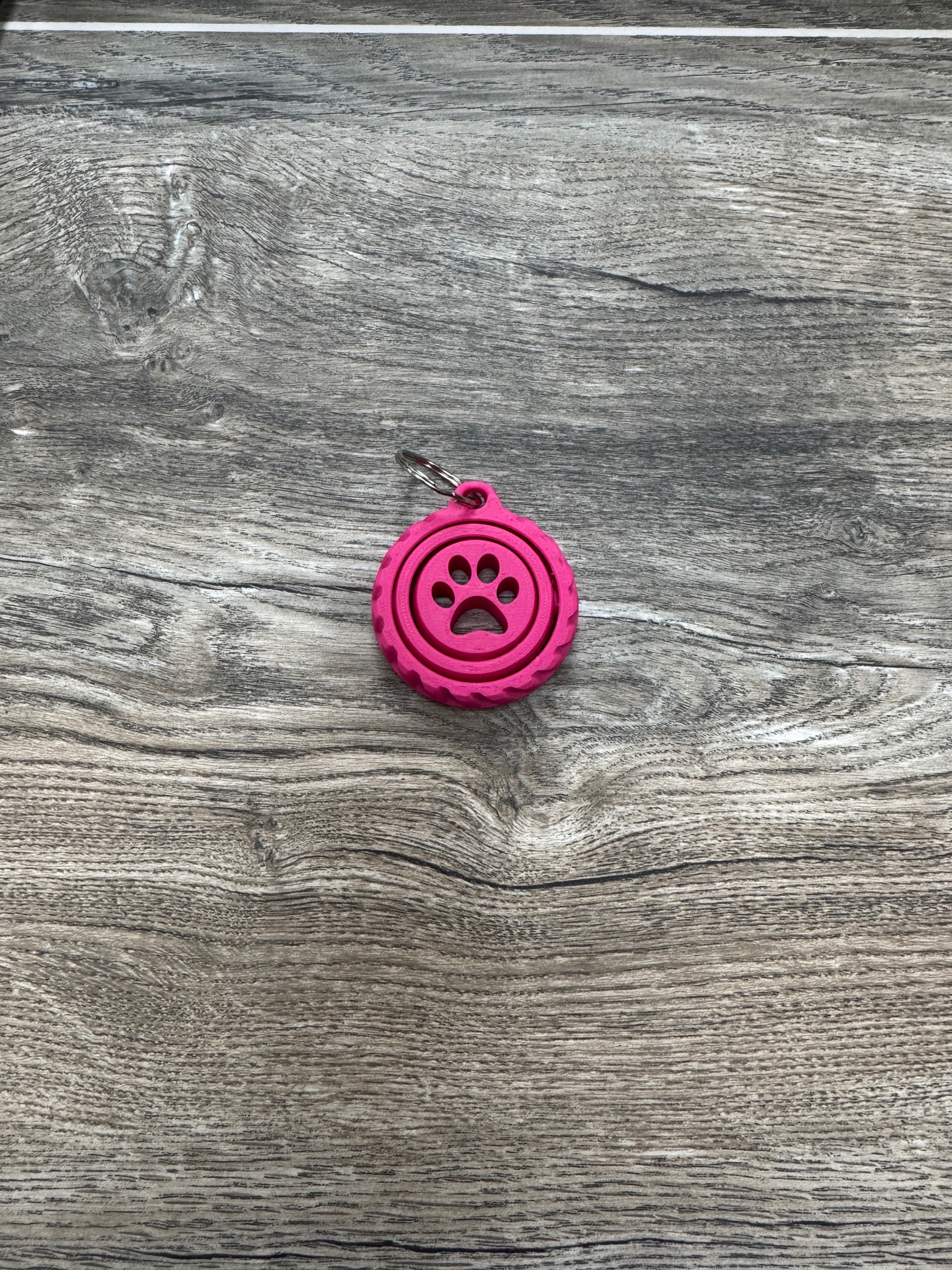 Hot pink fidget spinner keychain with a pawprint cutout in the middle.